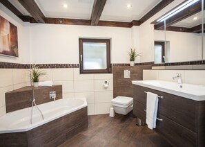 Ein modernes Badezimmer mit freistehender Badewanne, Toilette und Waschtisch mit Spiegel.