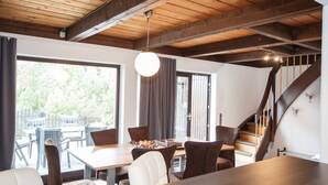 A dining area with a wooden table and chairs, a hanging light fixture, and a view of the outdoors through large windows. - Stylish Holiday Home near Winterberg with Private Sauna House, Terrace, & Garden (Winterberg)