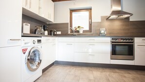 A modern kitchen with white cabinets, a stainless steel oven, a washing machine, and a window with a plant. - Stylish Holiday Home near Winterberg with Private Sauna House, Terrace, & Garden (Winterberg)