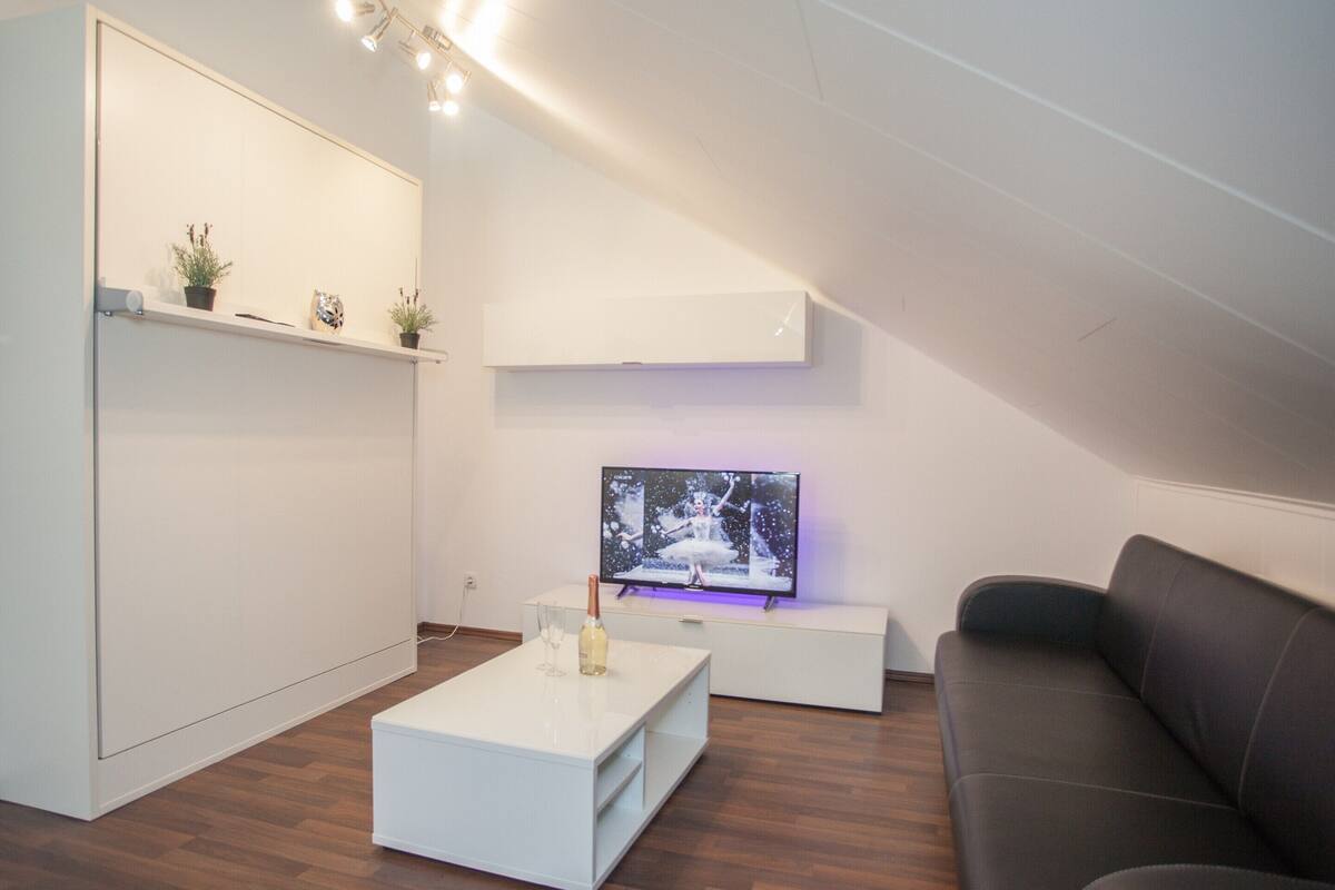 A modern living room with a flat-screen TV, a white coffee table, a gray sofa, and a white cabinet with shelves.