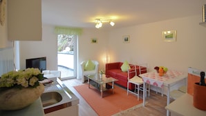 A living room with a sofa, coffee table, and a dining table with chairs. There is a TV and a window with a view of the outdoors. - Gruppenferienhaus im Sauerland (Schmallenberg)