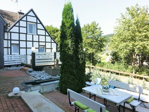 A traditional half-timbered house with a garden, outdoor seating, and a stone well.