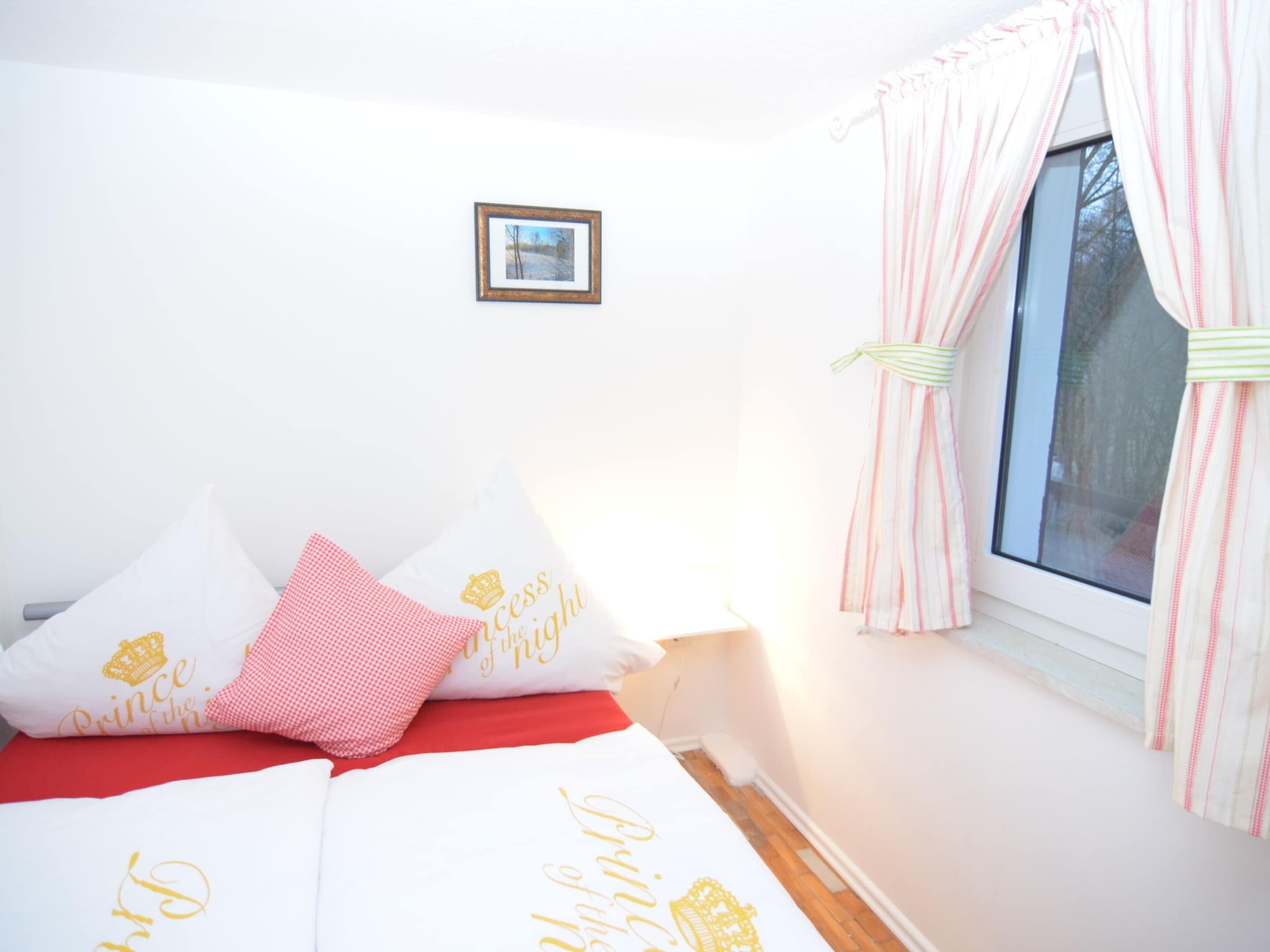 Un dormitorio con cama, almohadas, una ventana con cortinas y un cuadro en la pared.