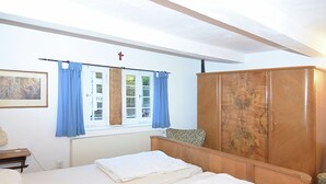A bedroom with two beds, a wooden wardrobe, a radiator, a window with blue curtains, and a painting on the wall. - Altes Ferienhaus mit Sauna in Heinsberg (Kirchhundem)