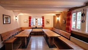 A room with wooden benches and tables, a fireplace, and a window with curtains. - Altes Ferienhaus mit Sauna in Heinsberg (Kirchhundem)