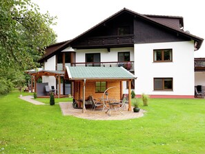 Un bâtiment à deux étages doté d’un patio couvert, d’une terrasse en bois et d’un petit jardin.