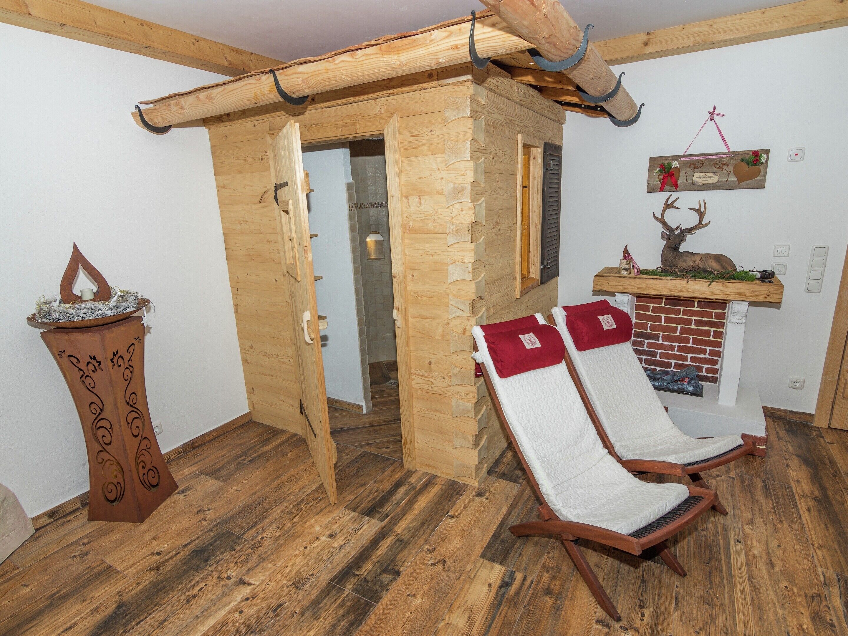 Ein Holzhütten-Interieur mit Kamin, zwei Liegesesseln, einer Holztür und einem dekorativen Geweih.