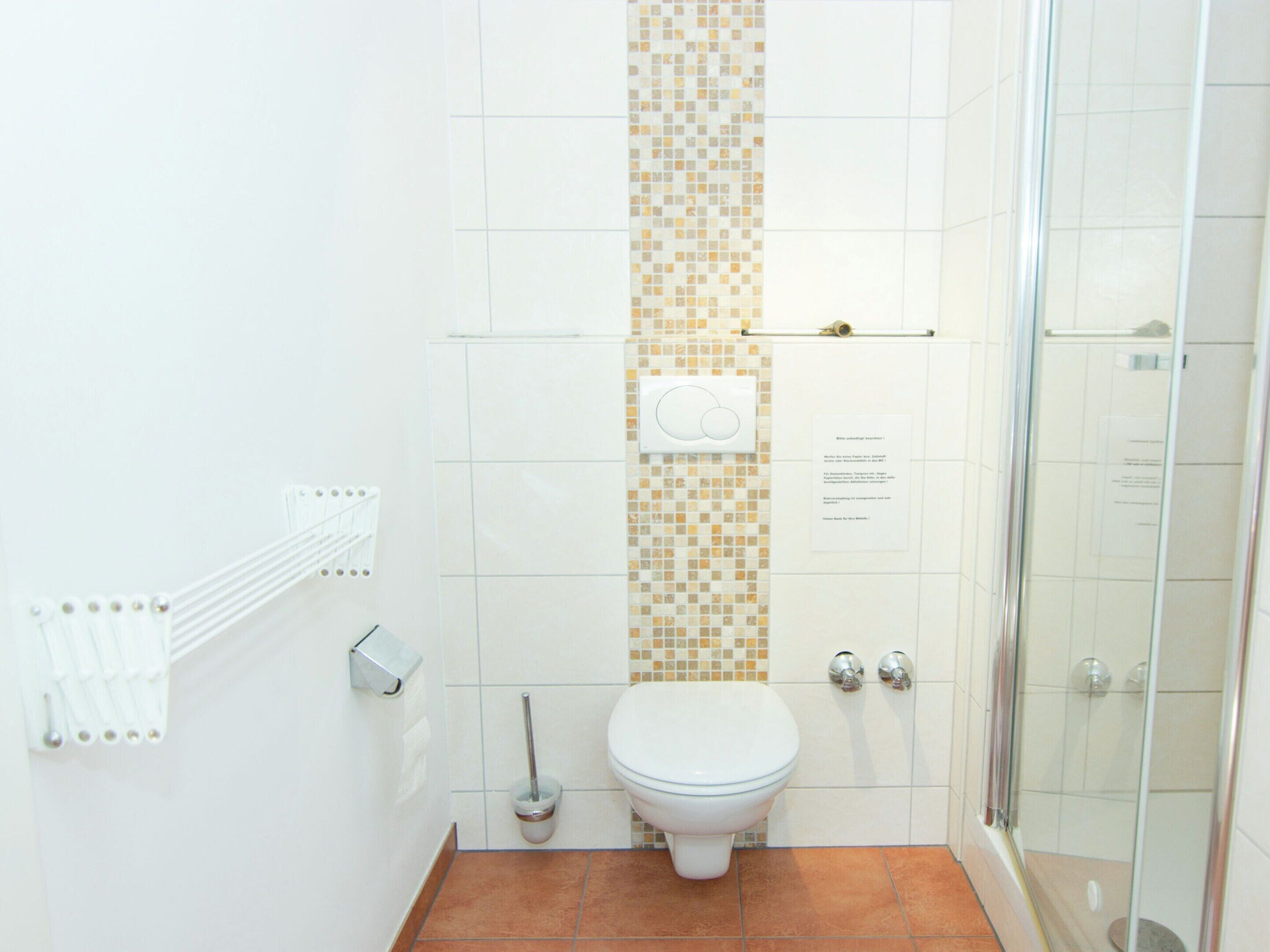 A bathroom with a toilet, a shower, and a tiled wall with a decorative pattern.