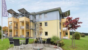 A multi-story building with a yellow and gray facade, outdoor seating area with chairs and a table, and a flag indicating it is an apartment hotel. - Apartment in Bad Durrheim Near Lake Constance (Bad Duerrheim)