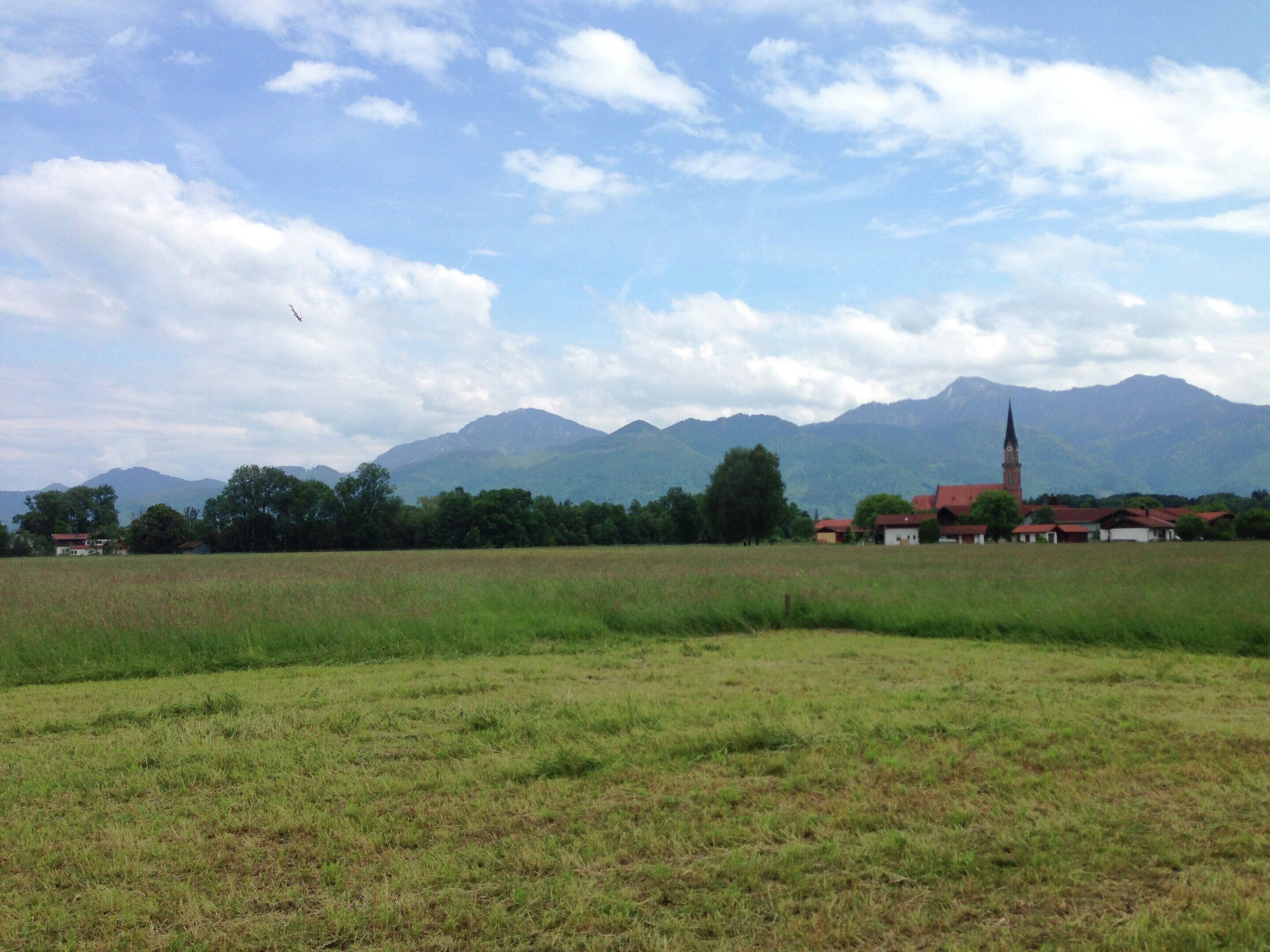 Un paysage rural avec une église et des maisons en arrière-plan, le tout entouré de montagnes.
