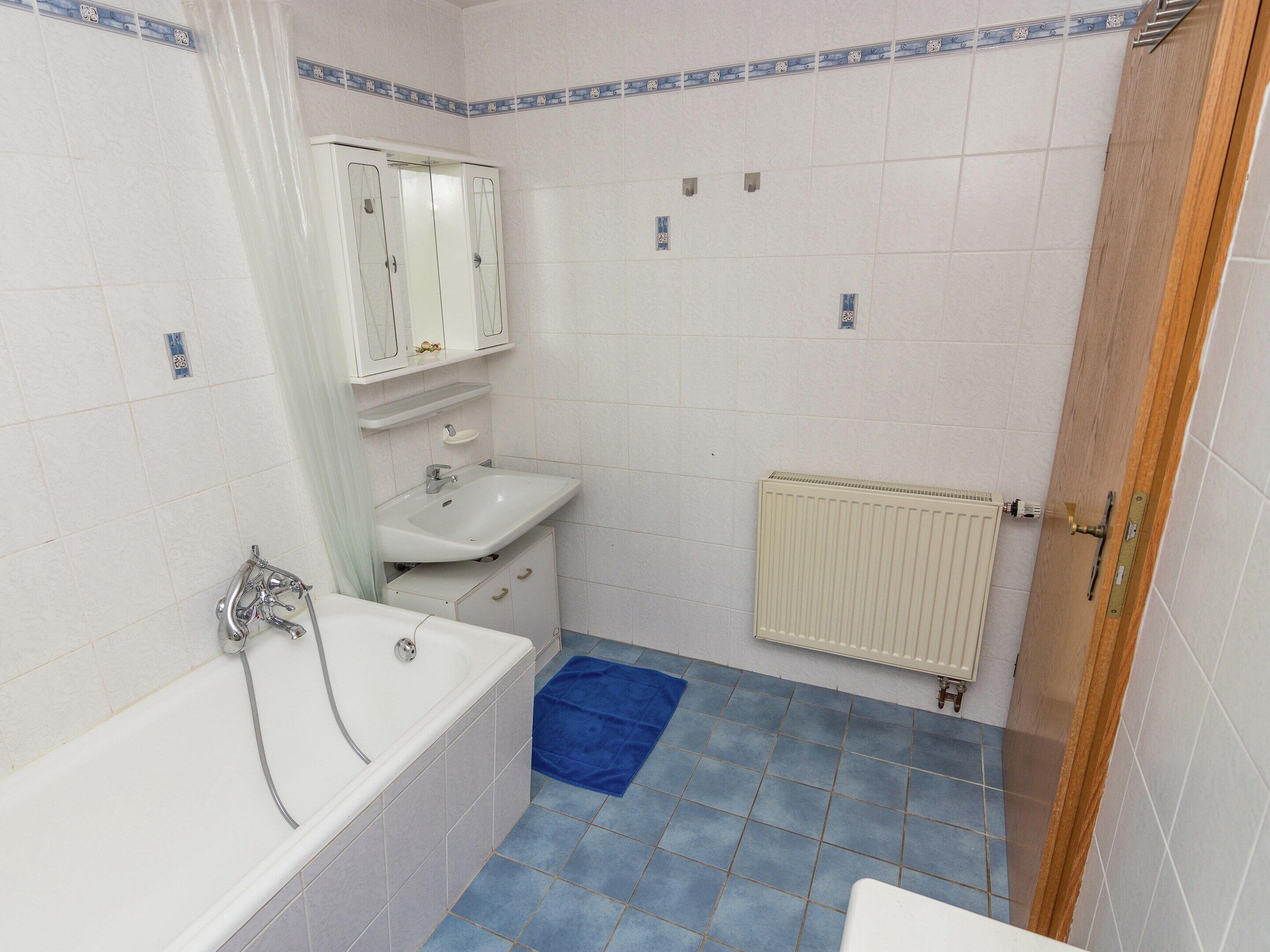 A bathroom with a bathtub, sink, and a radiator.