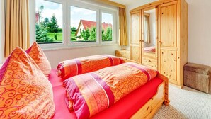 Un dormitorio con cama, dos ventanas, un armario y vistas al exterior con vegetación.