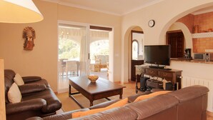 A living room with a sofa, a table with a bowl, a TV, and a kitchen area with a microwave. - Belvilla by OYO Mil Flores (Benissa)
