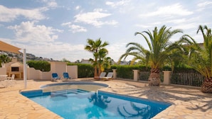 A swimming pool with stone tiles, surrounded by lounge chairs and palm trees. - Belvilla by OYO Mil Flores (Benissa)