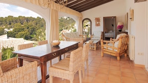A spacious room with a wooden dining table, wicker chairs, and a view of a lush landscape through large windows. - Belvilla by OYO Mil Flores (Benissa)