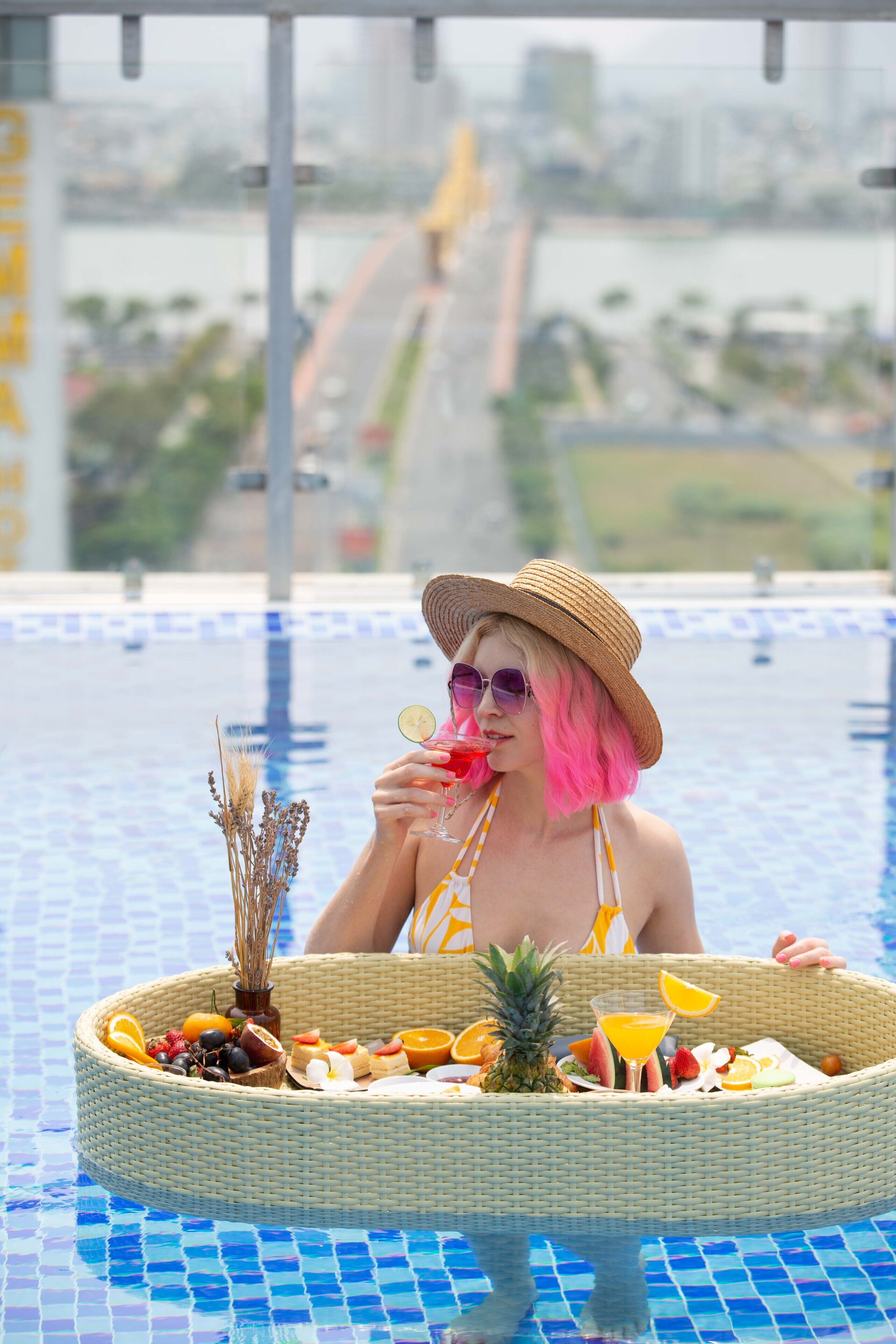 Eine Person sitzt am Pool mit einem Korbwägelchen voller Früchte und einem Getränk.