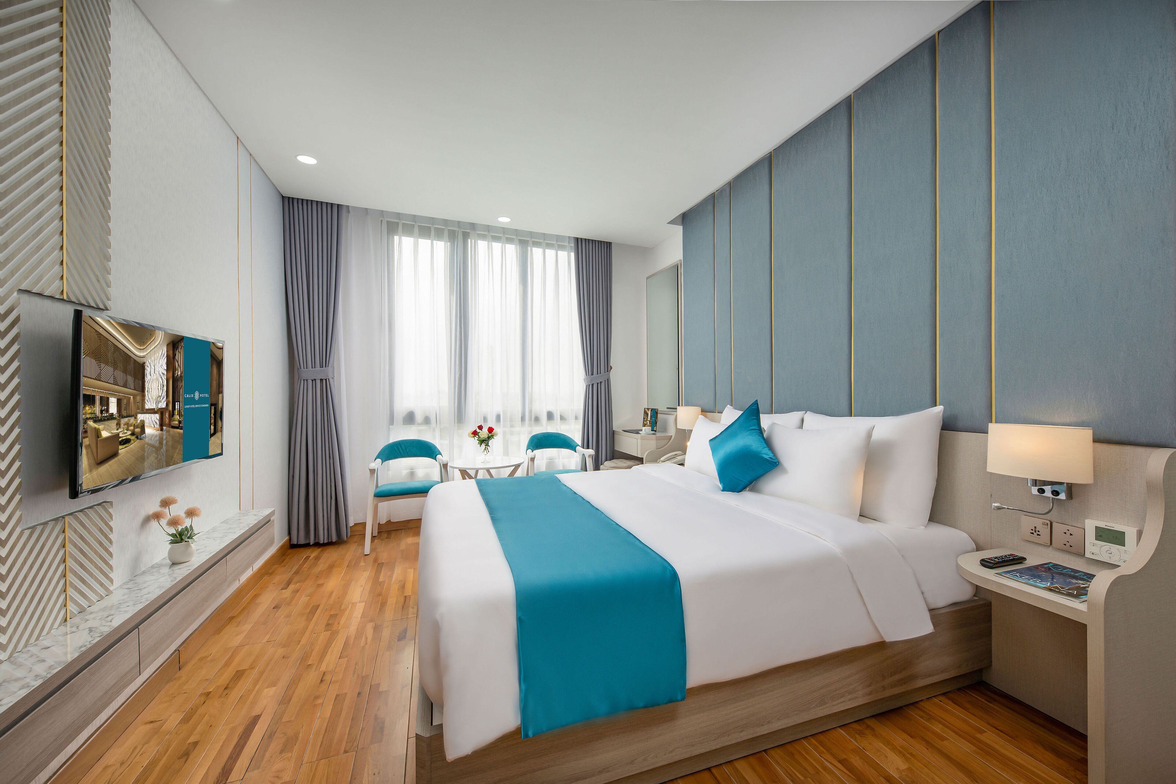 A modern hotel room with a large bed, a TV, a desk, and a seating area with chairs.