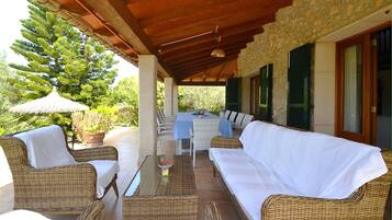 Un patio al aire libre con mobiliario de mimbre, una mesa con vela y vistas a follaje y un árbol.