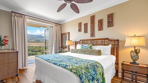 A hotel room with a large bed, a ceiling fan, a view of the landscape, and decorative wall art.