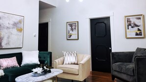 Una sala de estar moderna con un sofá verde, un sillón beige y un sillón negro. Hay una puerta negra, un techo blanco y un candelabro.