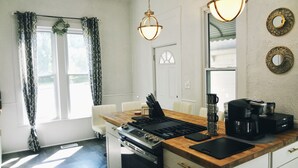 Una cocina moderna con encimera de madera, estufa a gas, cafetera y una zona de comedor con una silla blanca.