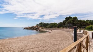 Una playa arenosa con un camino de madera y un afloramiento rocoso al fondo.