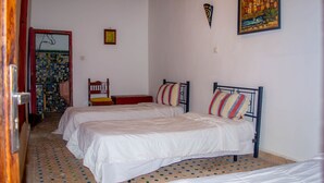 A room with two beds, a chair, a small table, and a door leading to another room. - La casa dar Rayan  (Fes)