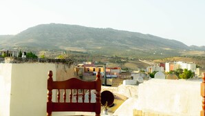 A wooden chair on a rooftop overlooking a cityscape with buildings and a hill in the background. - La casa dar Rayan  (Fes)
