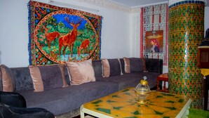 A living room with a sofa, a coffee table with a decorative bowl, a tapestry with a deer, and a colorful pillar. - La casa dar Rayan  (Fes)