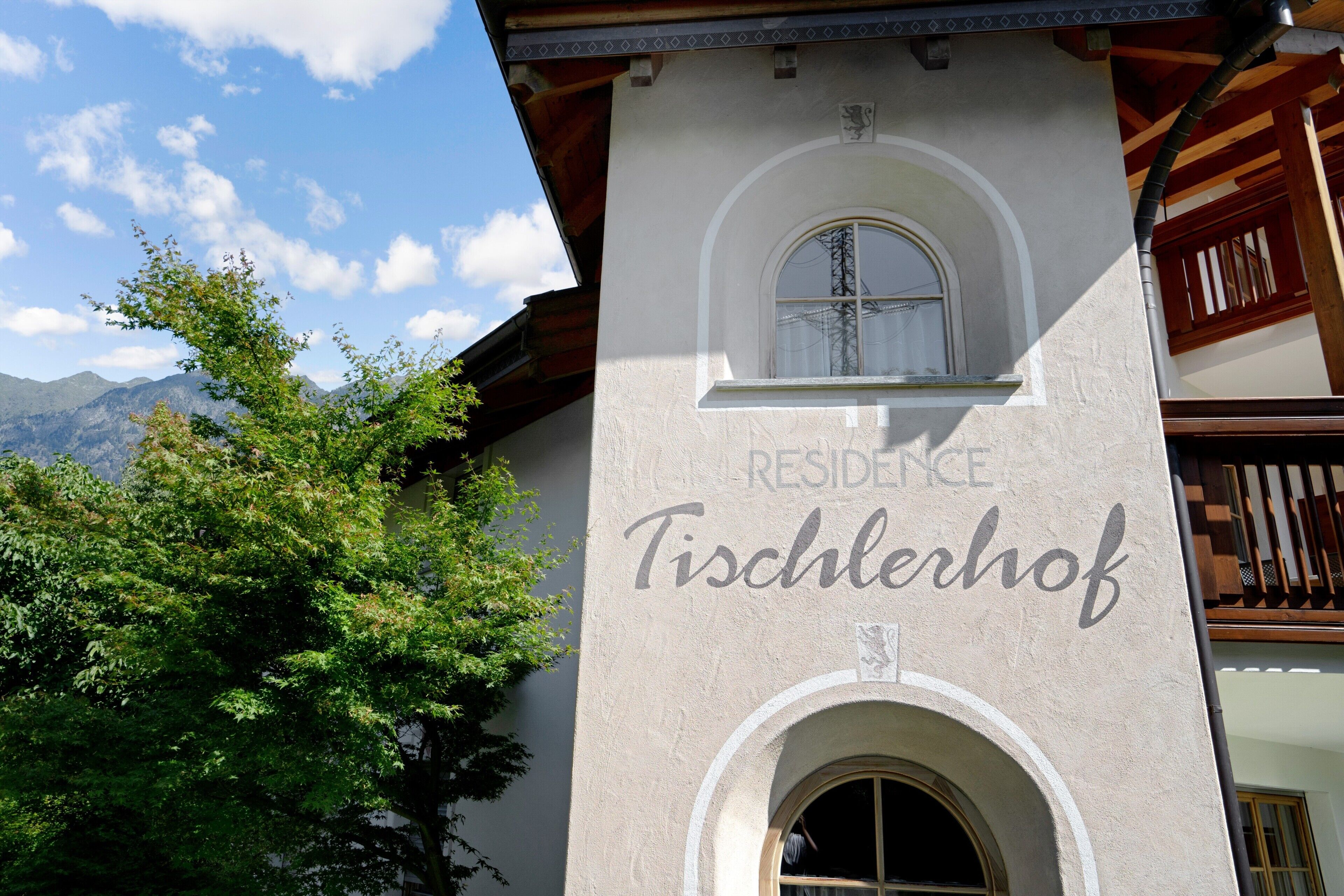 A building with a sign reading 'RESIDENCE Tischlerhof' and a window with a view of mountains.