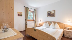 A wooden bed in a room with a window, a bedside table, and a nightstand. - Holiday Apartment "Tischlerhof - Typ B" with Wi-Fi, Terrace and Mountain View (Dorf Tirol bei Meran)