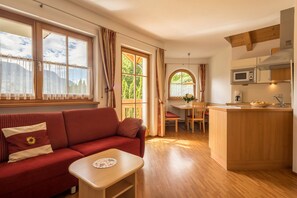 A cozy living room with a red sofa, a small wooden table, and a view of the outdoors through large windows.