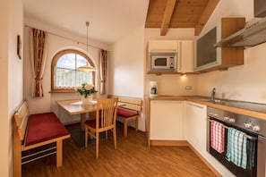 A compact kitchen with a dining area, wooden flooring, and a window with curtains.