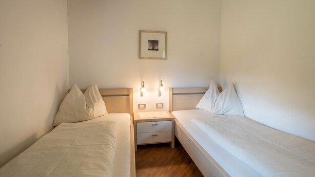 Ett hotellrum med två separata sängar, ett nattduksbord med en lampa och en inramad tavla på väggen.