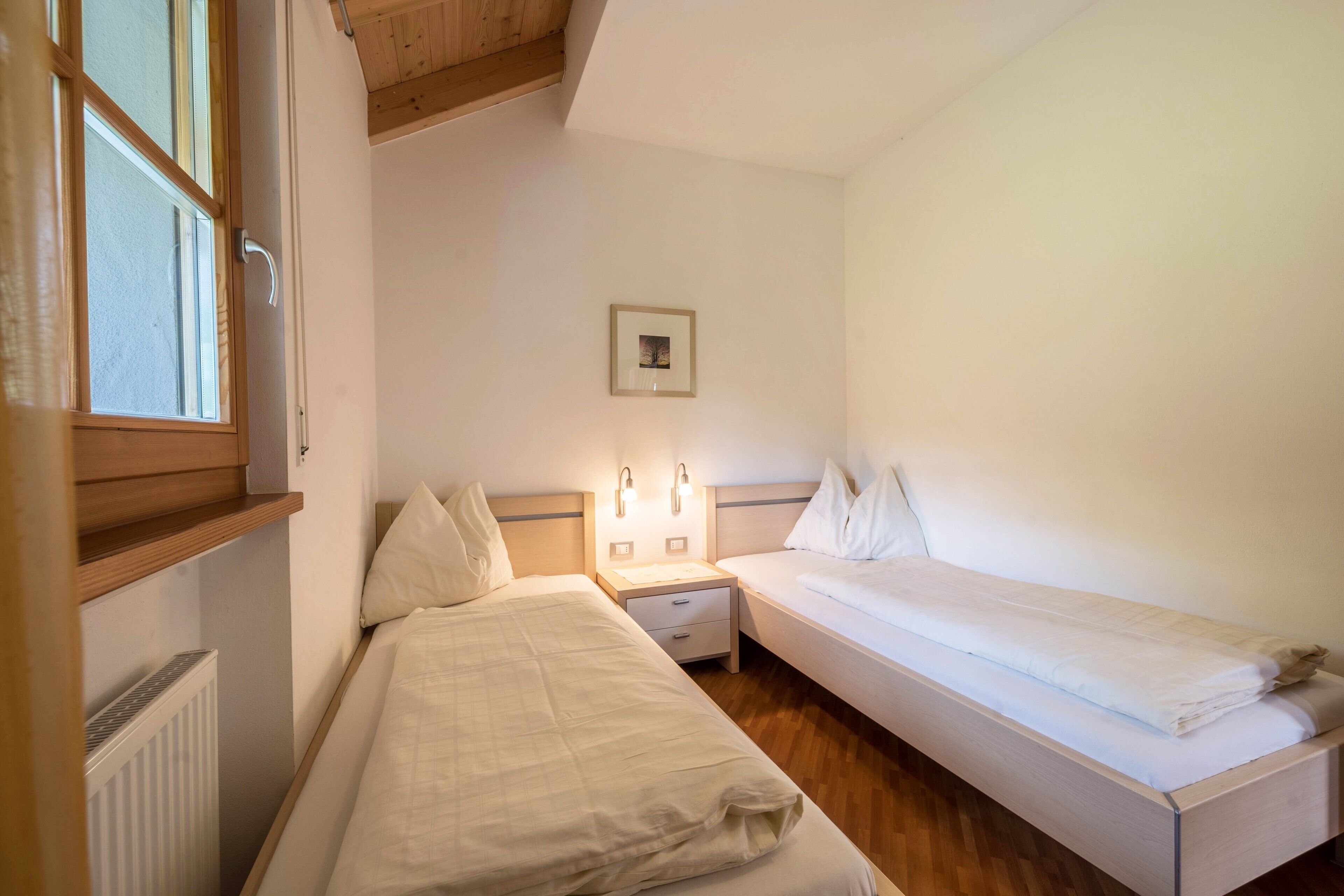 Una camera da letto con due letti singoli, un comodino, un quadro appeso al muro e una finestra con persiane.