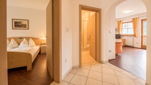 A bedroom with a bed, bedside tables, and a nightstand. There is a bathroom with a toilet and sink. The room has a tiled floor and a wooden door.