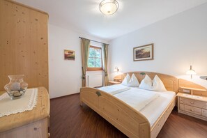 Un lit en bois dans une pièce avec une fenêtre, une table de chevet, une commode et une lampe fixée au mur.