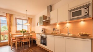 A modern kitchen with a dining area, wooden cabinets, a microwave, and a window with curtains.