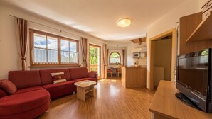 Una sala de estar moderna con un sofá rojo, suelo de madera, un televisor y una cocina con microondas.
