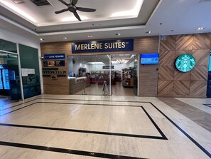 A hotel entrance with a reception desk, a sign reading "MERLENE SUITES™", and a Starbucks logo on the wall. - Mansion One Suites By Merlene (George Town)