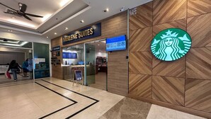 Un vestíbulo de hotel con un mostrador de recepción, un letrero que dice Merlene Suites y el logotipo de Starbucks en la pared.