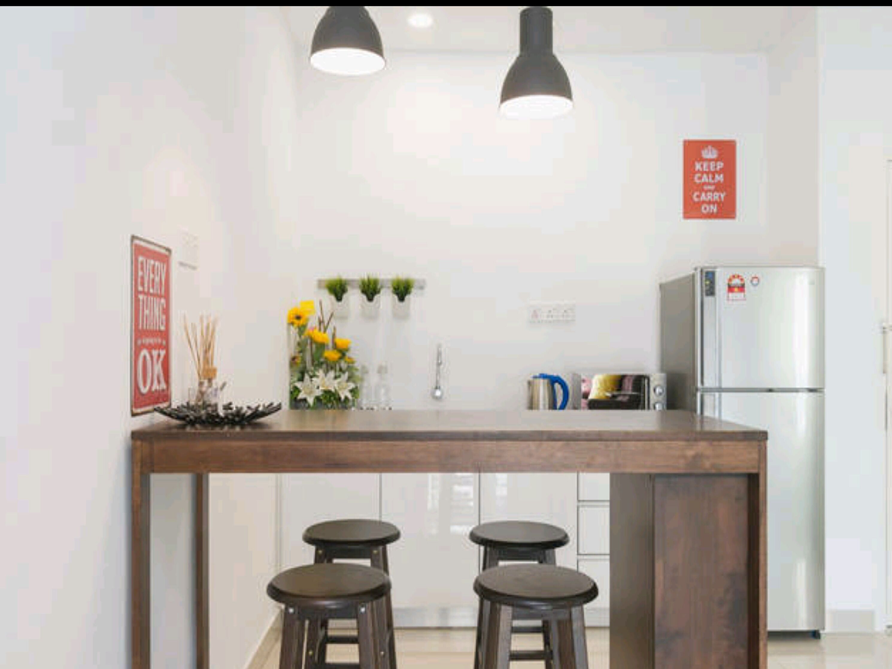 A modern kitchen with a central island, two bar stools, pendant lighting, and a refrigerator.