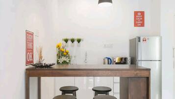 A modern kitchen with a central island, two bar stools, pendant lighting, and a refrigerator.