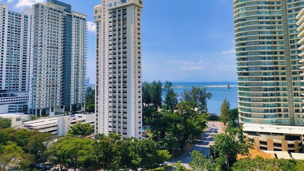 Un edificio residencial alto con varios balcones, rodeado de vegetación y una vista despejada del océano.