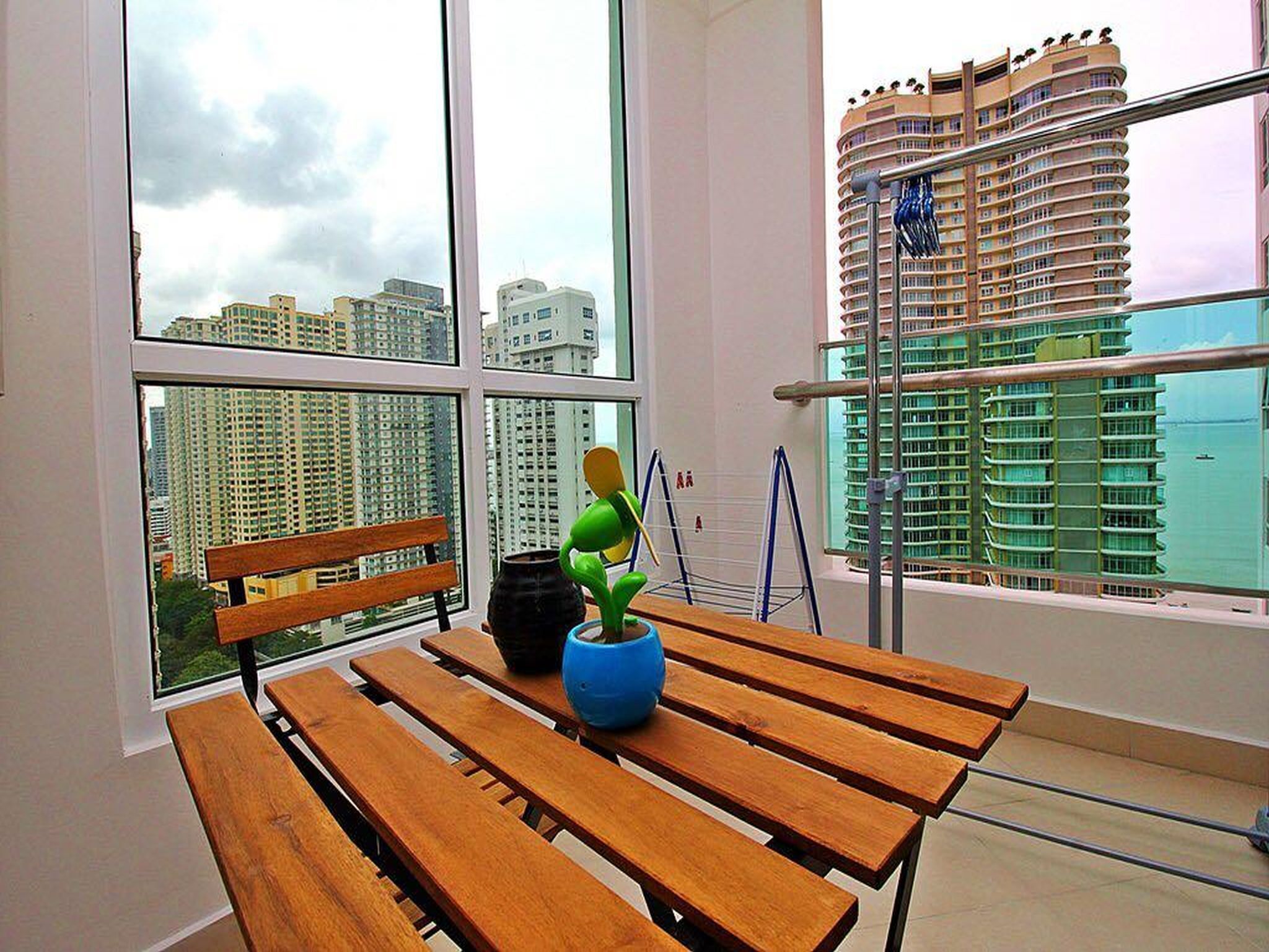 Ein Balkon mit einer Holzbank, einer blauen Vase mit Pflanze und einem Metallgeländer.