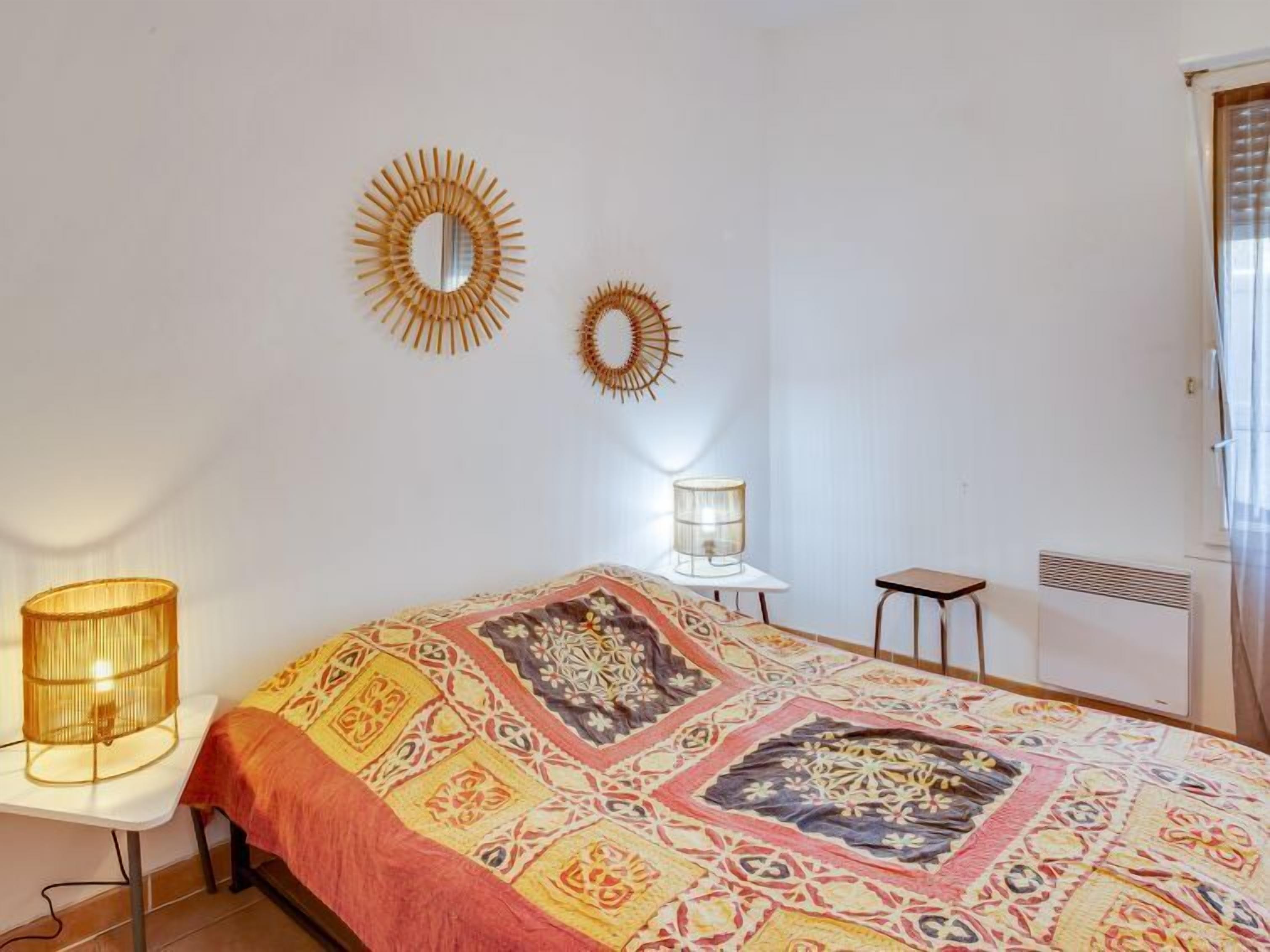 Un dormitorio con una colcha estampada, dos espejos en la pared, una lámpara de noche y un radiador.