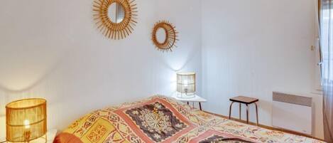 Un dormitorio con una colcha estampada, dos espejos en la pared, una lámpara de noche y un radiador.