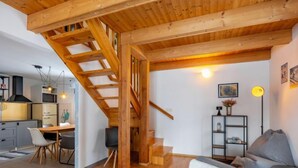 Een modern interieur met een houten trap, een eethoek en een zithoek met een bank en een lamp.