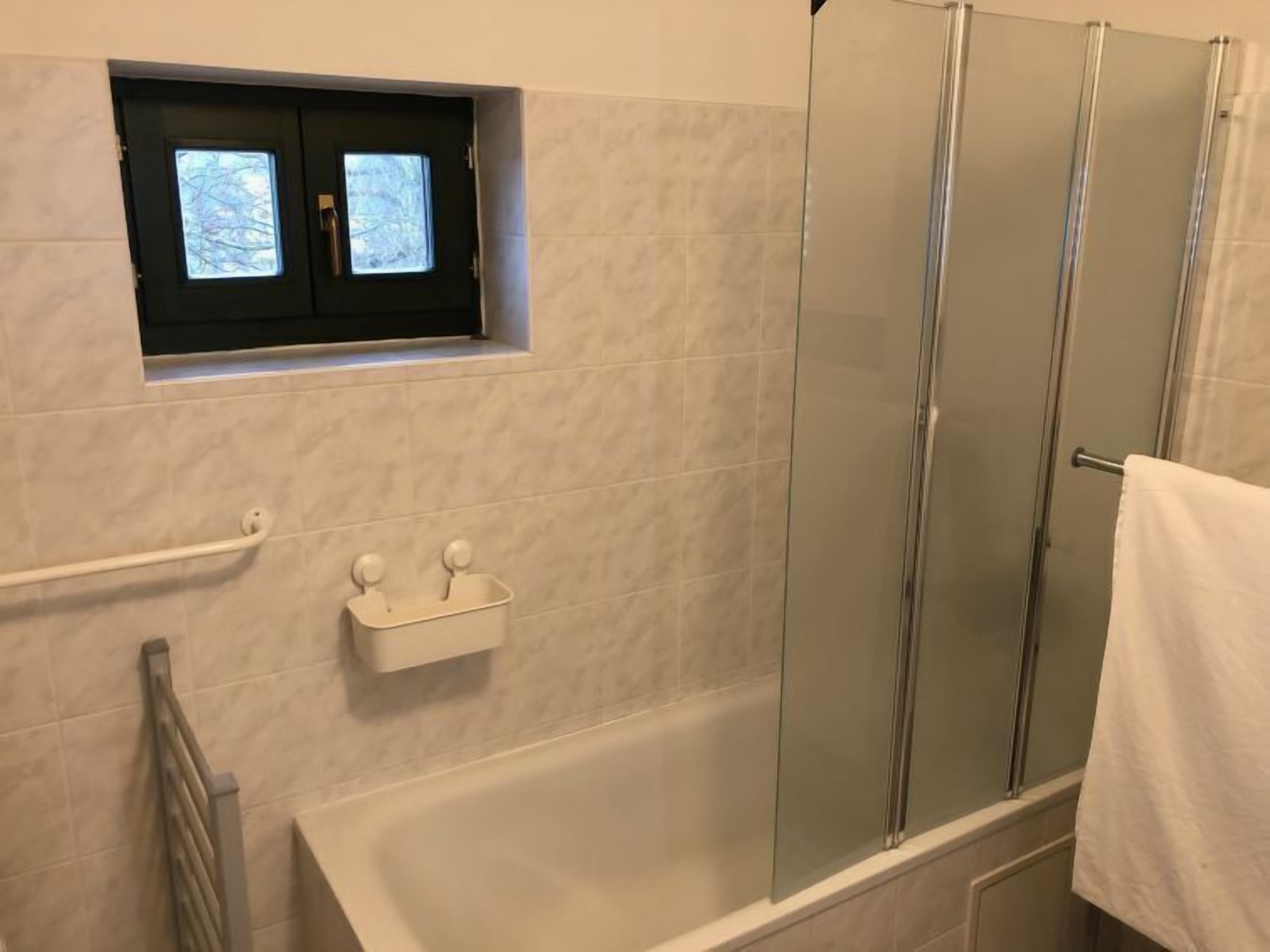 Een badkamer met een bad, een douche met glazen wanden, een raam en een handdoekhouder.