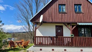 Een houten huis met twee verdiepingen, een balkon, een schotelantenne en een kleine tuin met een tafel en stoelen.